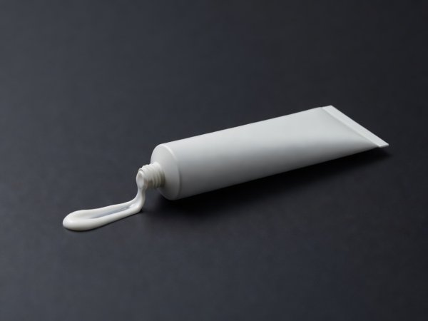 Soft-lit 3D render of a single clinical sunscreen tube with a measured strip of white emulsion on a dark surface